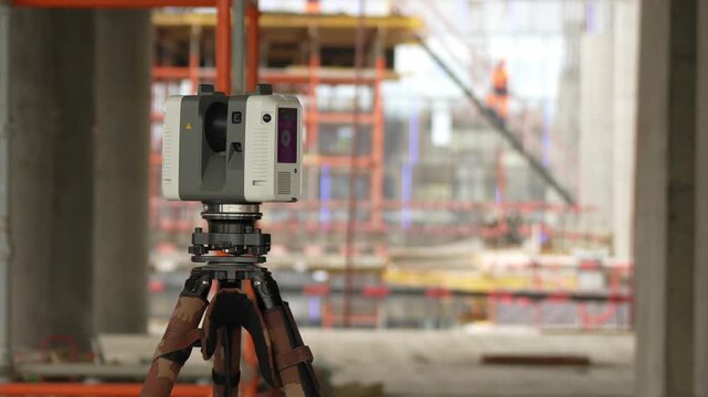 Gray laser theodolite sits securely on a wooden tripod. Blurred scaffolding and steel beams form the construction backdrop. Surveyors rely on this equipment for accurate site measurements