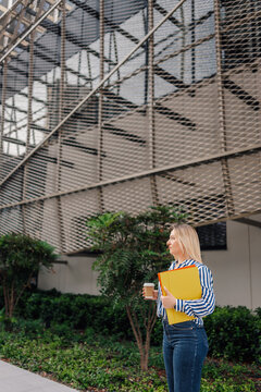 Businesswoman walking with coffee and folders outdoors