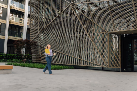Businesswoman walking outdoors holding folder and coffee