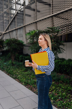Woman walking with coffee and folders in city
