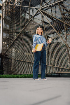 Businesswoman standing in city with coffee and folder