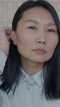 Slow motion portrait of pensive Asian woman looking at camera against glass wall background. Emotion and expression concept.