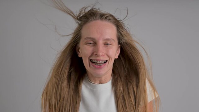 A portrait of a Caucasian woman with braces. A sudden gust of air flutters her hair.