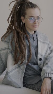 Slow motion portrait of young woman with dreadlocks sitting on sofa in luxury apartment looking at camera. People and interior concept.