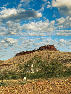 Outback landscape featuring red rock hill and scattered clouds