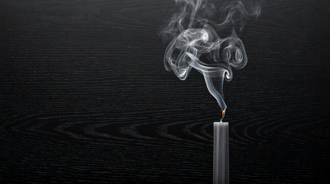 Grey smoke curls upward from a freshly snuffed tall taper candle against dark background