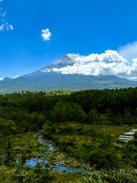 Mount semeru volcano with clouds over river and forest