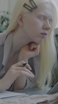 Albino woman student learning online surfing internet and writing in notebook studying from home in bed. Distance education and people concept.
