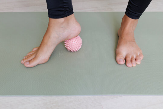 Bare foot presses a spiky massage ball under the arch during preventive foot exercise for plantar fascia release, arch mobility, muscle activation and sole stimulation.