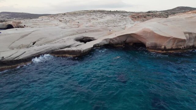 Wide drone aerial view of white volcanic arch rock formations bordering dark blue sea on Milos Island, Greece. Scenic natural moonscape of Sarakiniko.