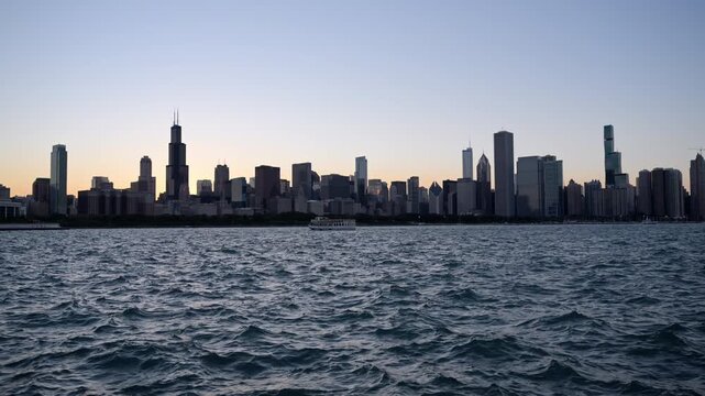 Chicago skyline viewed across Lake Michigan at dusk, featuring downtown skyscrapers and the Willis Tower silhouetted against the evening sky.