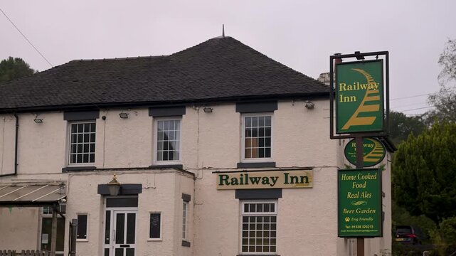 Static shot of the Railway Inn pub frontage and roadside hanging sign under grey skies.