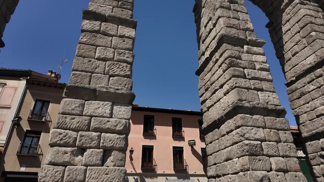 Dynamic handheld shot captures the towering stone arches of the Segovia Aqueduct as numerous swifts fly around, set against a deep blue sky and warm daylight, emphasizing ancient grandeur.