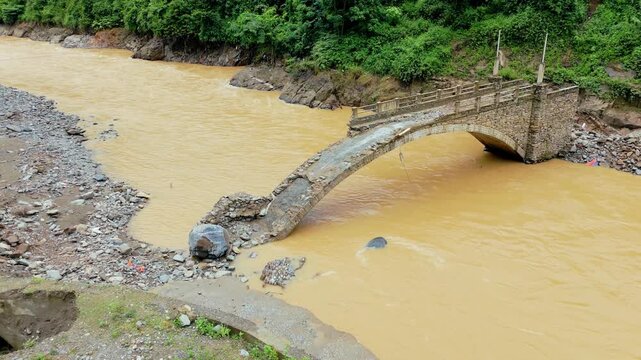 Flood muddy water sweeping large bolder destroys bridge in valley during heavy rain season, north Vietnam.