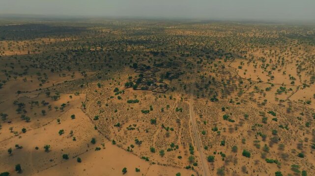 High drone panorama over the Thar Desert in Sindh, Pakistan, showing scattered rural compounds, sandy tracks and patchy thorn vegetation across an expansive semi-arid plain.