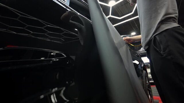 Close up footage of process installed vinyl wrap on a car body in a workshop. detailing process with film installation, smooth matte finish and precision work