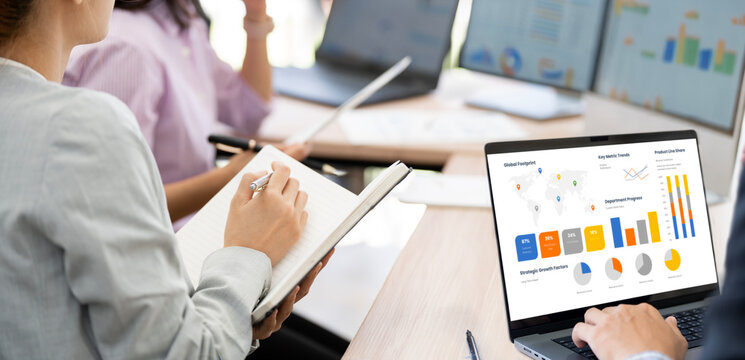 Businesswoman holding notebook and taking notes during laptop presentation in office.