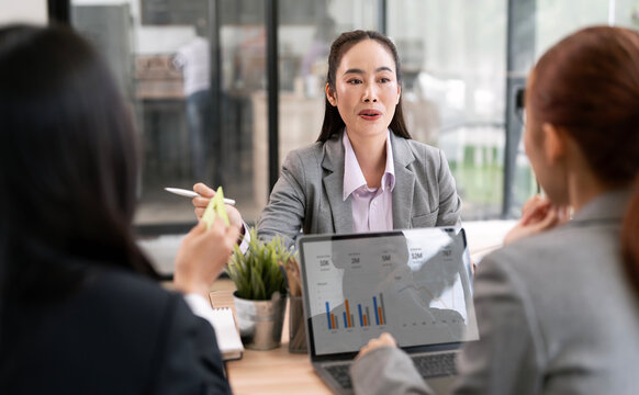 Asian businesswoman presenting financial charts and data on laptop during team meeting.
