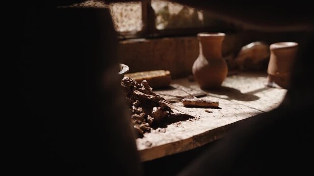 Ancient rustic pottery and artifacts on a wooden table, illuminated by a ray of light, evoking historical and traditional settings