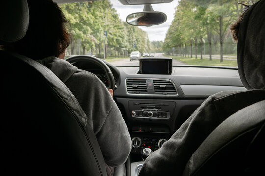 Rear seat view of a couple in hoodies driving together on a scenic tree lined city street for a weekend road trip concept