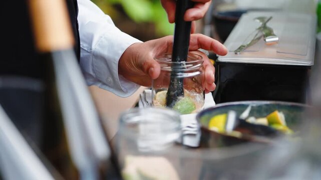 Bartender hands muddling fresh lime and sugar in a glass, preparing a vibrant cocktail or mojito drink