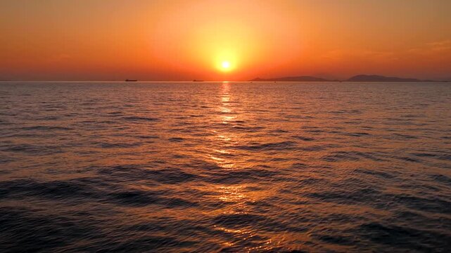 Aerial pov captains view of a flight over calm ocean during a beautiful sunset with orange and red sunlight and reflections in the water