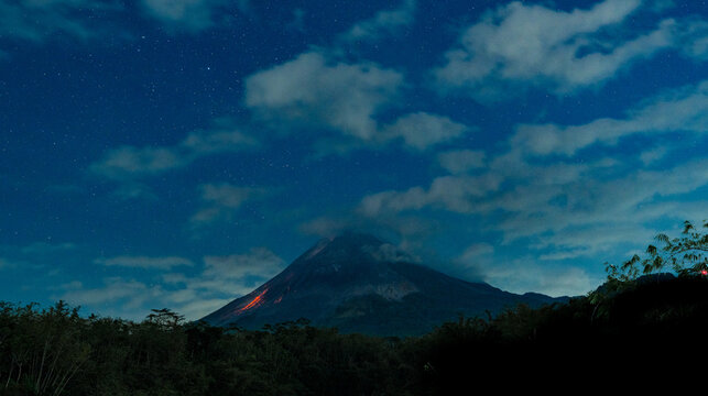 Mount merapi volcano erupting lava under starry night sky