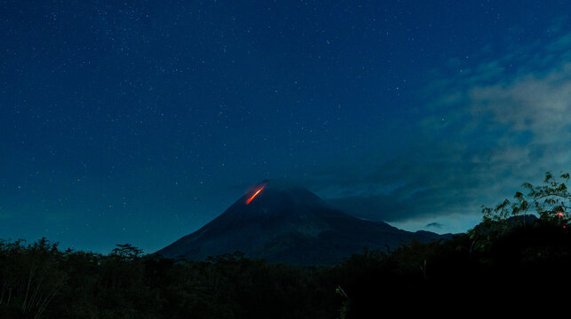 Mount merapi volcano erupting lava under starry night sky