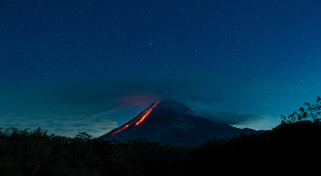 Mount merapi volcano erupting lava at starry night