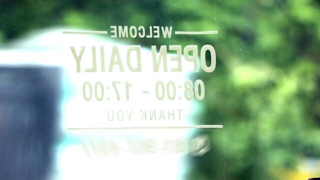 Mirrored white vinyl sticker on glass door showing welcome open daily opening hours sign