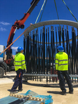 Workers installing wind turbine foundation anchor cage using crane