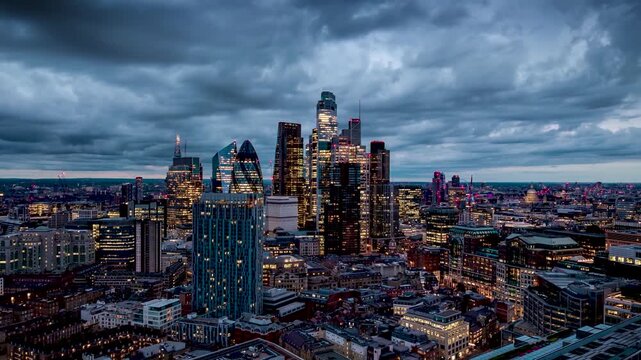 Hyper timelapse view of the illuminated office skyscrapers and the skyline at the City of London, England, during a moody evening with clouds