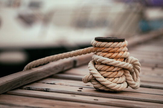 Close-up of a thick nautical mooring rope securely wrapped around a metal bollard on a wooden pier.