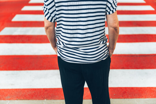 Back view of a woman wearing a striped shirt standing before a vivid red and white pedestrian zebra crosswalk.