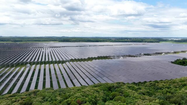 Aerial view of large scale solar power station surrounded by lush green vegetation fields