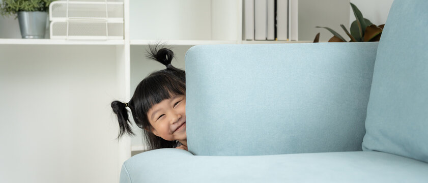 little asian children kid playing hide and seek standing behind the sofa, Adorable child having fun in the home. happy family have fun with kids, activity, learning, activity, game, meditation