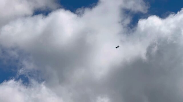 A high altitude silhouette view of a jet aircraft flying through white clouds.
