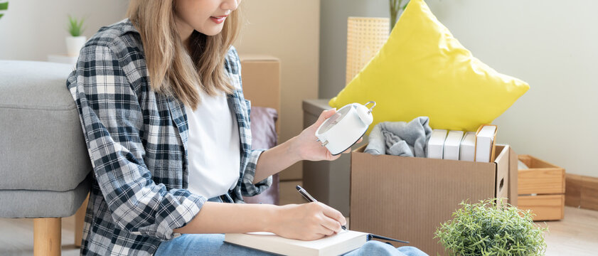 Move house, relocation. Woman using household checklist for new apartment Inside the room are cardboard boxes containing personal belongings and furniture. Move into a house or condominium