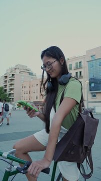 Young asian woman using smartphone while sitting on bicycle