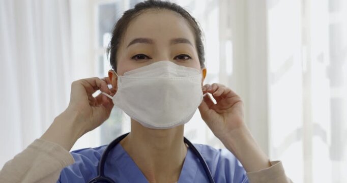 Healthcare professional wearing blue scrubs adjusting protective face mask in a bright clinical setting, emphasizing infection prevention and safety. Medical wellness concept
