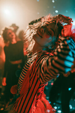 Clown at Halloween Costume Party Energetic Woman Dancing in Striped Outfit Under Colorful Lights During Night Celebration
