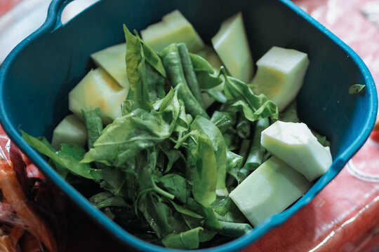 top-down view of fresh green vegetables and chopped light-green chayote squash served inside a dark blue container.