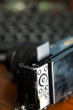 close-up view of a memory card being inserted into a digital camera slot, with a blurred keyboard in the background.