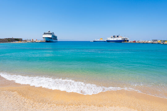 Beach with yellow sand and turquoise sea in Rhodes, Greece. Cruise ship and ferries in the port.