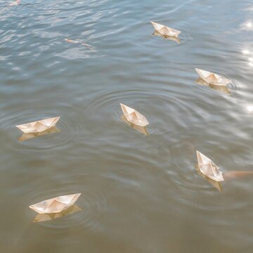 Paper boats floating on calm water, delicate folded ships drifting on a soft blue surface for anti bullying and social exclusion concepts
