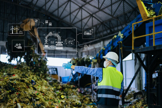 Asian engineer in hardhat using tablet with green energy and carbon neutral HUD graphics inside recycling factory