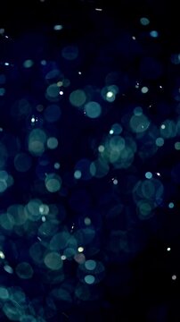 Glowing bokeh particles. Abstract blue particles drift softly through dark space, creating dreamy bokeh and glittering light specks in fluid, futuristic style with calm motion.