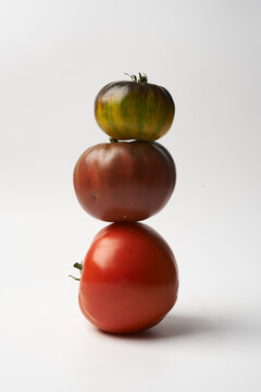 Three colorful heirloom tomatoes stacked on top of each other against a white background, still life food photography