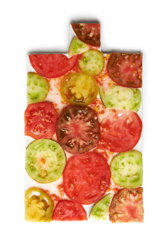 Colorful heirloom tomato slices of different varieties arranged in a pattern on a white cutting board, top view food photography