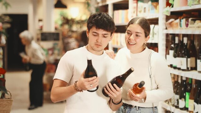Joyful couple of lovers choose dry or sweet wine in a hypermarket, standing in the department with alcohol against the background of customers . High quality 4k footage